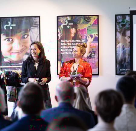 To damer står foran en forsamling og snakker.