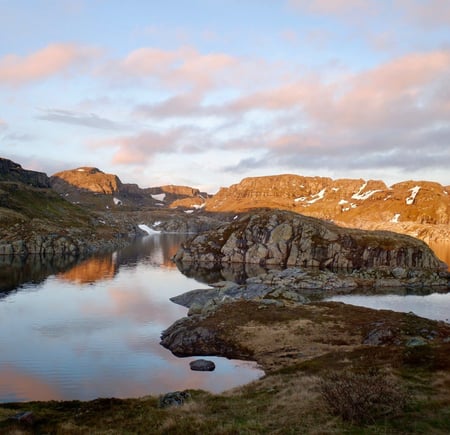 Morgenstemning med soloppgang over et stille vann i fjellet. Det ligger litt snø enkelte steder 