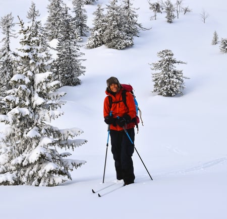 Kvinne i rød jakke står i hvitt snøkledd landskap med ski på beina.