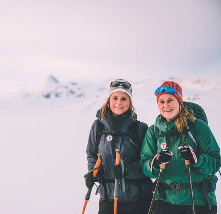 To smilende damer på ski på vinterfjellet.