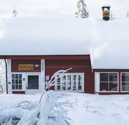 Mann foran en rødmalt hytte med mye snø på taket