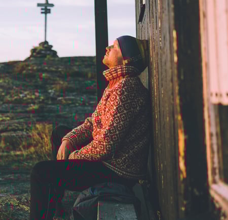 Mann i rød genser som sitter med solen i hytteveggen