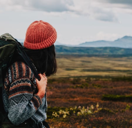 Person med sekk og oransje lue som ser utover fjellet