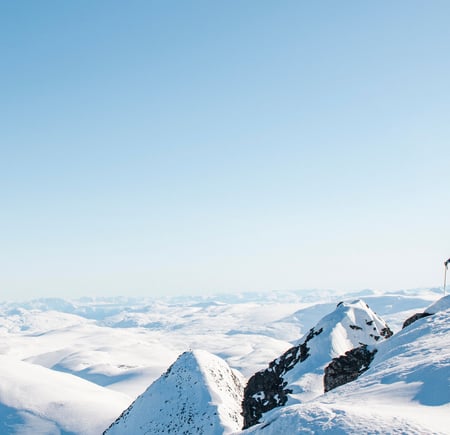 To personer med ski på sekken på en snødekket fjelltopp