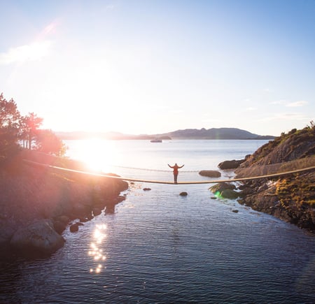 Dronebilde av hengebru på Vassøy i Stavanger. En person står i midten av broen og strekker armene ut.