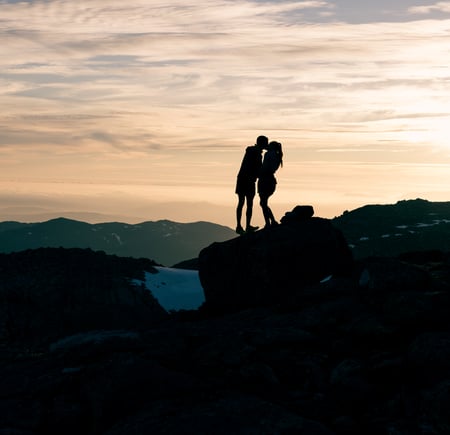 Kjærestepar kysser i solnedgang på fjelltopp.