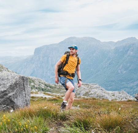 En mann i gul t-skjorte og shorts går på toppen av et fjell.