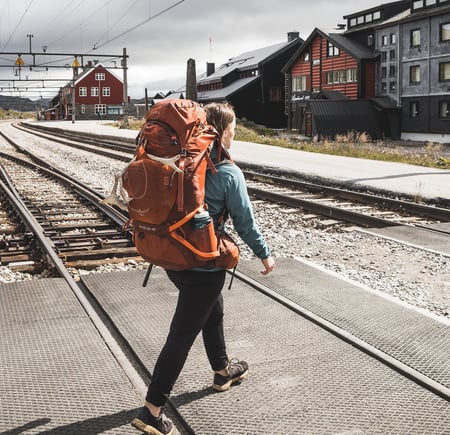 Person med ryggsekk som går over toglinjer.