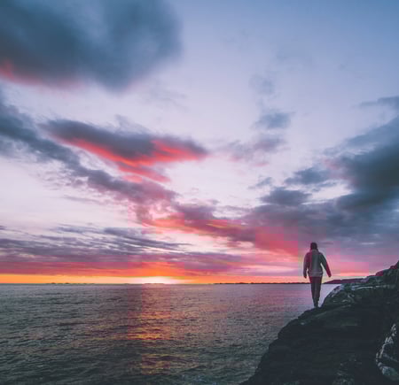 en person som står på en klippe og ser på solnedgangen