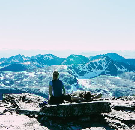 To personer som ligger på en stein og ser utover et fjellområde