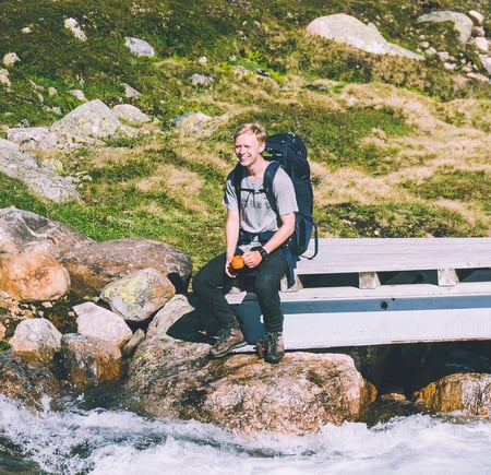 En person som sitter på en bro ved en elv i fjellet