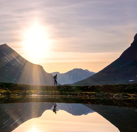 Person som går i fjellet med solnedgang i bakgrunnen