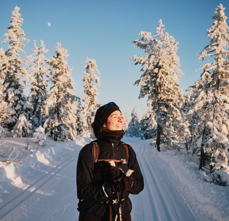 Smilende kvinne på ski i snødekt skog.