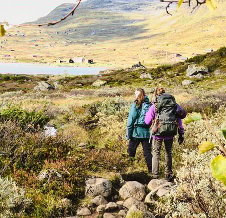 To personer med sekk som går på en sti i grønt fjellterreng