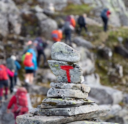 Tød T malt på varde i høyfjell med turgruppe i ufokus bak.
