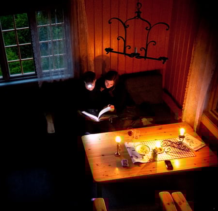 To personer som sitter ved et bord med levende lys og hodelykt og leser.