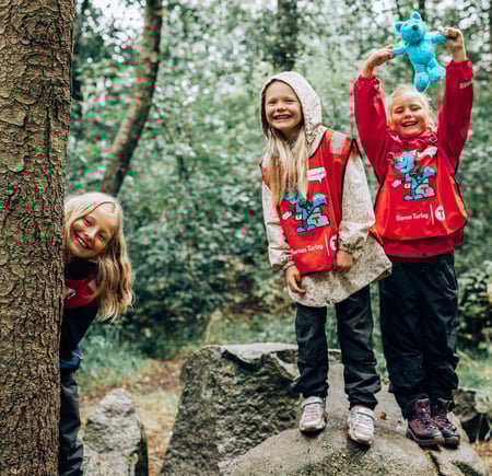 Tre jenter leker i skogen med blå Turbo-bamse