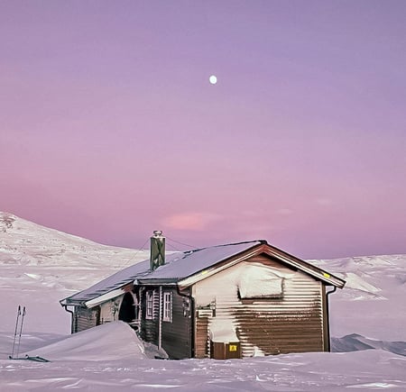Bjellåvasstua dekket av snø og under rosa vinter himmel.
