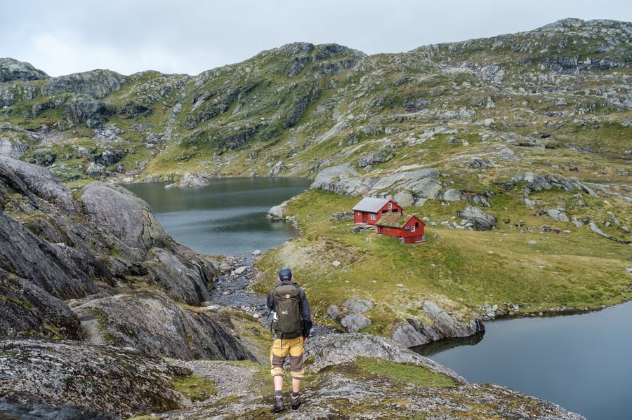 Mann med turklede står og ser på raud hytte i fjelllandsskap