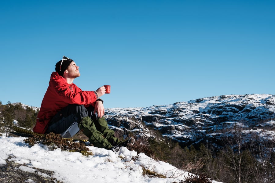 En mann sitter på toppen av et fjell og nyter en kopp kaffe i solen
