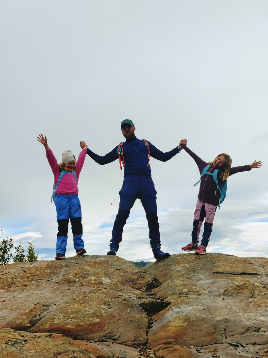 To barn og en voksen holder hender på en fjelltopp