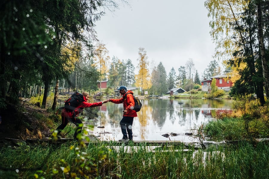 To personer på tur, den ene hjelpes over en bekk.