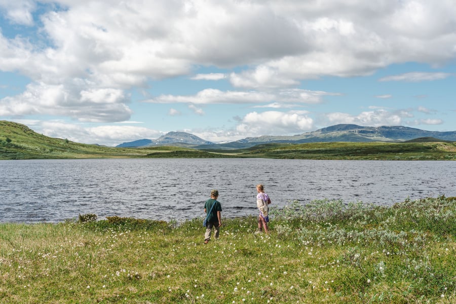 To barn ved et fjellvann og fine fjelltopper bak.