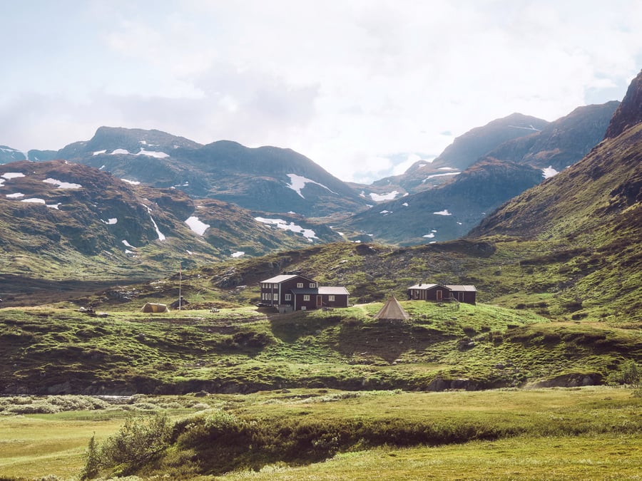 Sommerfjell med vakre grønnfarger, vi ser en hytte midt i bildet.