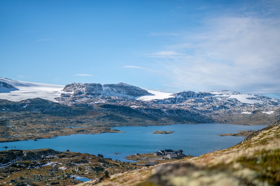 Utsikt over blått fjellvann med vakre snødekte fjell bak.