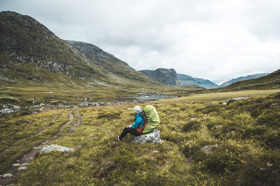 Turgåer som sitter og hviler på en stein, i vakkert fjellterreng.