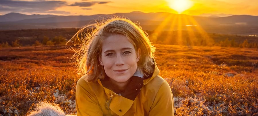 Kvinne ligger på en sovepose med solnedgang i bakgrunn