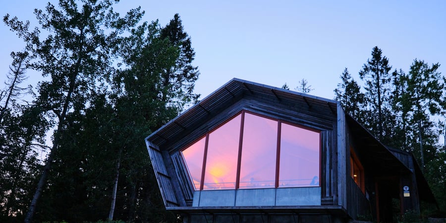 En hytte med store glassvinduer og solnedgang som reflekteres i vinduene