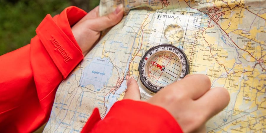 En person med rød jakke holder kart og kompass.