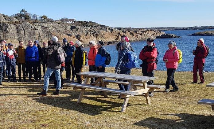 Mennesker og benk på grasslette ved sjøen