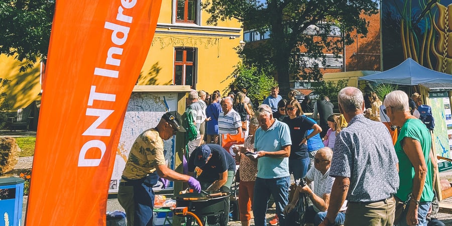 Det grilles pølser på stand med mange besøkende – et DNT Indre Østfold beachflagg står i front.