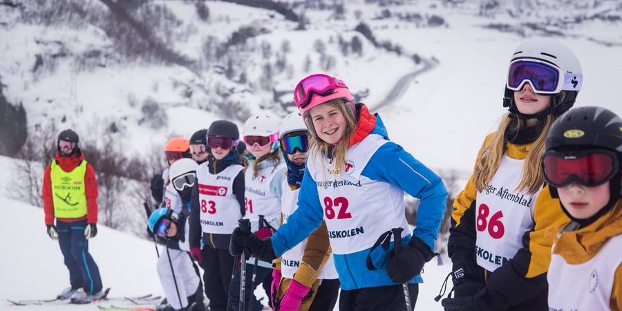 Deltakere på skiskolen ser inn i kamera, stående på rekke i skibakken