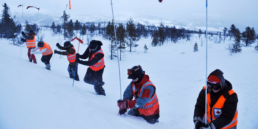 Flere personer i oransje vester graver i snøen.