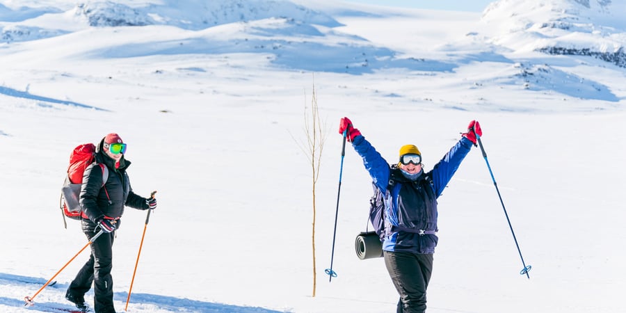 To skigåere i vinterfjellet, den ene holde armene opp i været