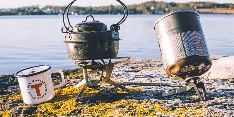 Kaffekopp, primus og kjele står på et svaberg med sjøen bak. 