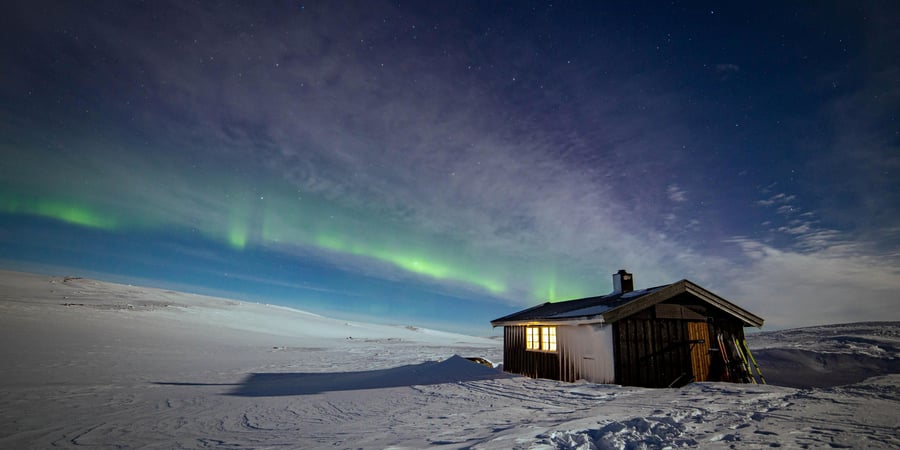 Liten hytte med nordlys skinnende over hytta
