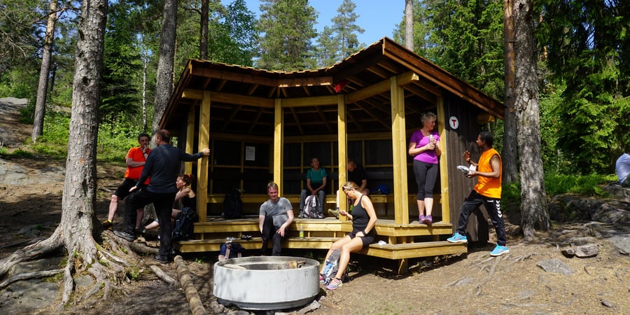 Gapahuk i skogen med sitteplasser og bålpanne.