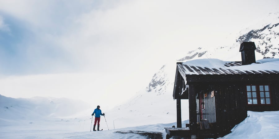 Person på fjellski utenfor en svartmalt hytte 