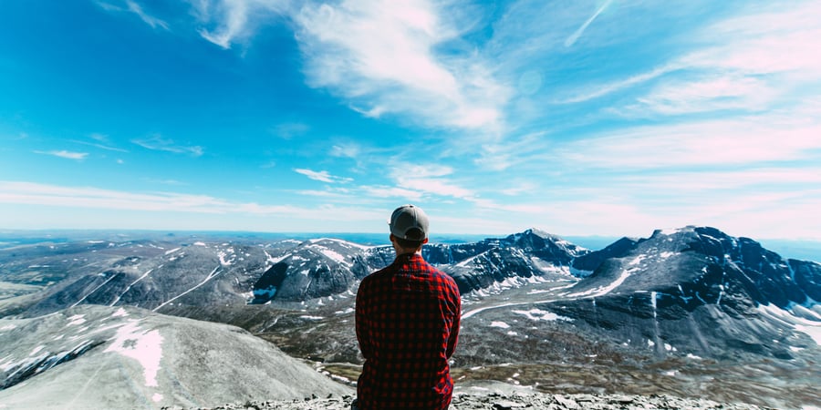 Mann i rød og sort skjorte som ser utover et fjellområde