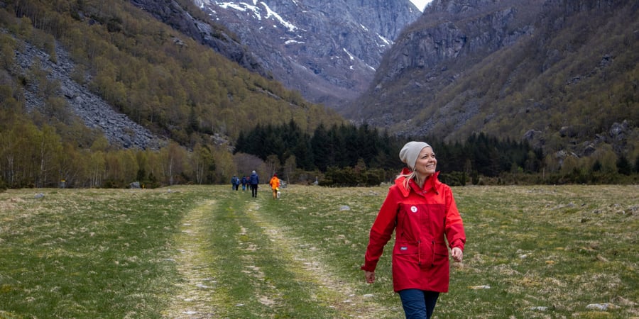 En dame i rød jakke som går tur inne i en dal.