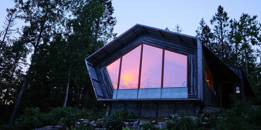 En hytte med store glassvinduer og solnedgang som reflekteres i vinduene