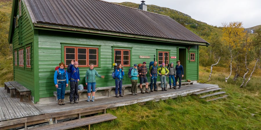 En gjeng med voksne turgåere står foran grønn hytte.