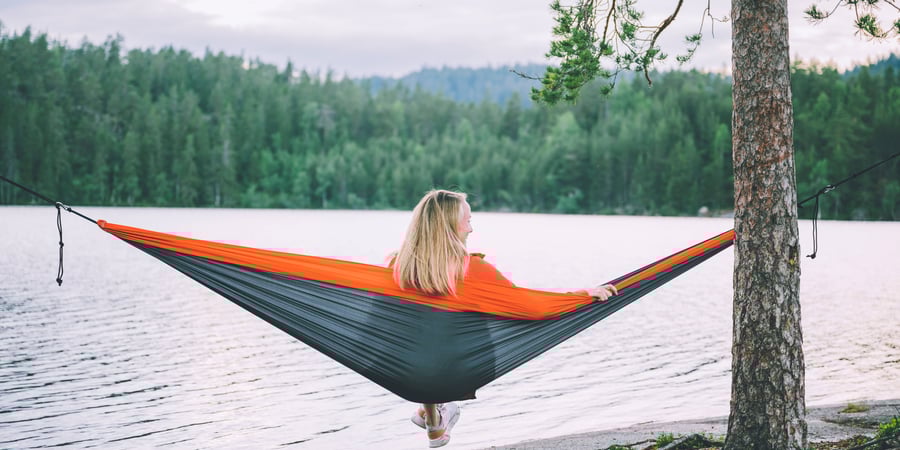 Kvinne som sitter i en hengekøye og ser utover et vann