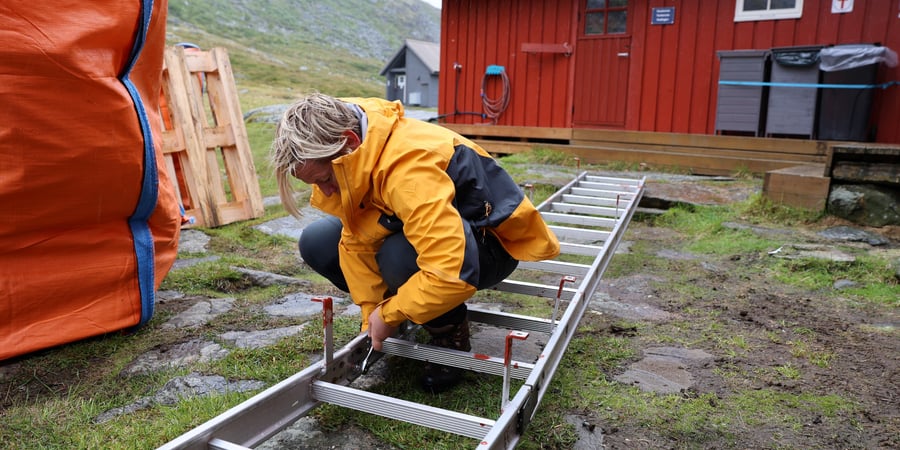 Person jobber med en stige foran hytte.