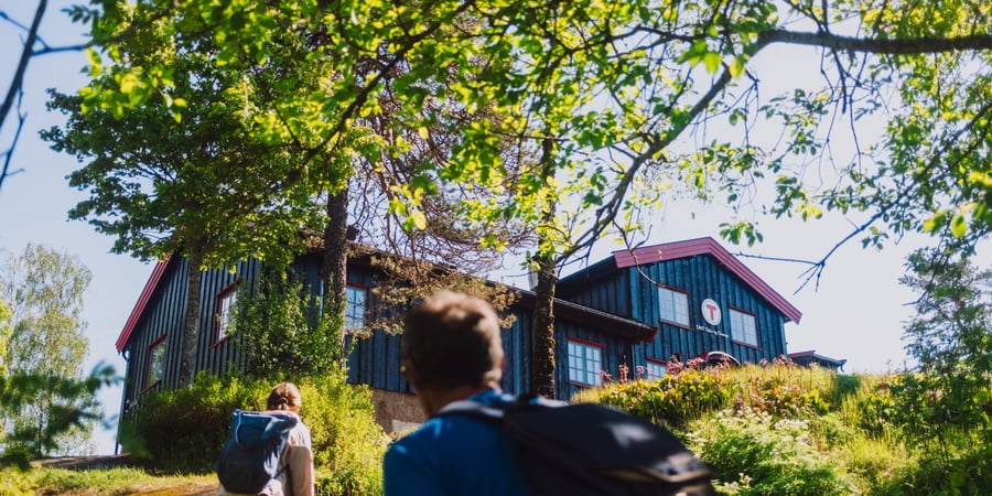 To personer som går mot en svartmalt hytte