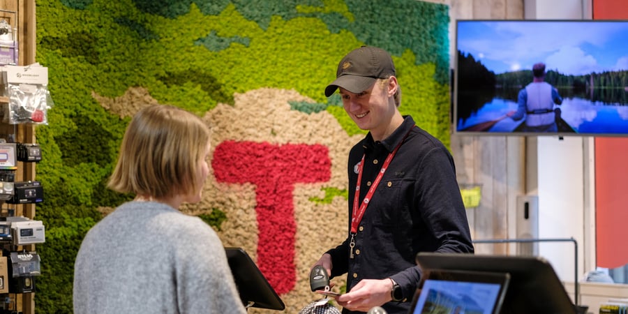 En mann som står bak en butikkdisk og snakker med en dame
